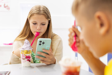 boy and a girl eat ice cream in a summer cafe in a summer cafe,a girl looks at a photo on her phone