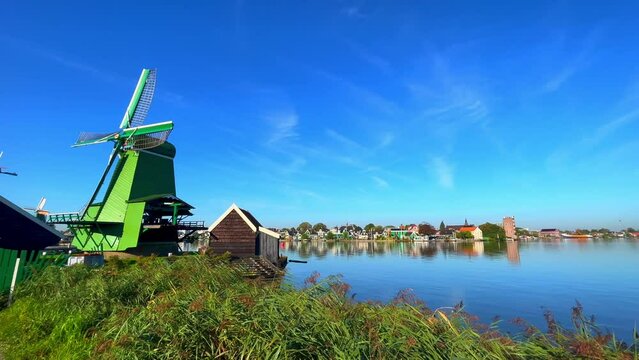 Green Dutch mill next to Zaan river and village houses at Zaanstad