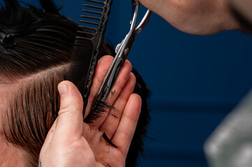 Focused Caucasian male hairdresser cuts a Caucasian guy's hair in a beauty salon. hairdresser at work, blue background, haircut with a typewriter and scissors. 