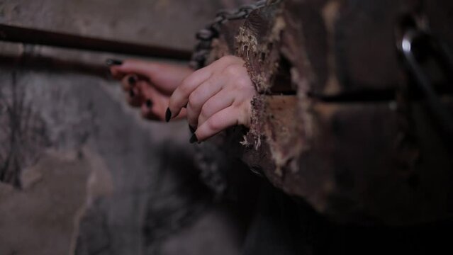 Close-up of a young woman's hands in antique wooden shackles with a chain in a dark room. Quest room with creepy tasks for adults. A room of fear or horror.