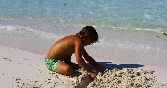 A young Caucasian boy is digging in sand on Cocoplum Beach on Exuma in the Bahamas.