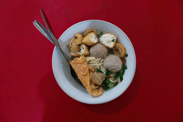 A bowl of soup containing noodles, meatballs, fried tofu and dumplings