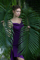 Outdoor portrait of stylish fashionable woman in purple silk dress in tropical resort. Natural light. Stylish, elegant summertime outfit, spring-summer fashion trend, tropical vacation style.