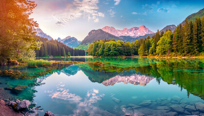Calm morning view of Fusine lake. Colorful summer sunrise in Julian Alps with Mangart peak on...