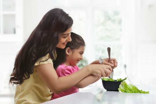 Young mother and daughter eating salad in the kitchen