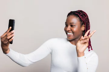 Foto op Plexiglas Happy cheerful attractive African American dark skinned woman with braids smiling showing two fingers at camera standing over white background in studio isolated having shooting process © ABCreative