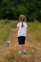 little girl on a dirt road waiting for her dog