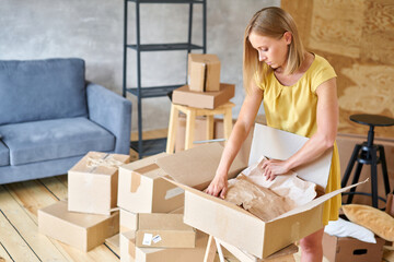 Young girl packing plates into the boxes ready to move. Woman unpacking moving boxes in her new...