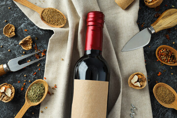 Glass bottle on towel and wooden spoons with spices on gray background, top view