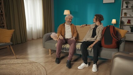 Shot of a teenager, young man sitting on a couch, sofa with his grandfather, granddad and talking...