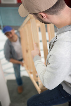 Men Carrying A Wooden Frame Up Flight Of Stairs