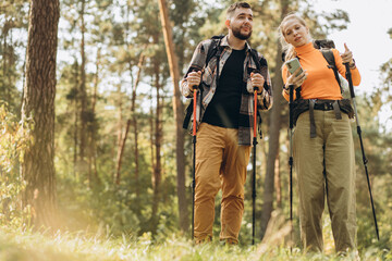 Naklejka na ściany i meble Couple hiking with bags and walking sticks in forest