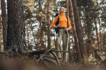 Woman hiking with walking sticks in forest stopped by the tree