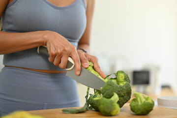Young woman cutting fresh broccoli on chopping board, preparing healthy meal in kitchen