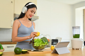 Beautiful young woman preparing fresh healthy vegan salad in the kitchen at home. Dieting and healthy lifestyle concept