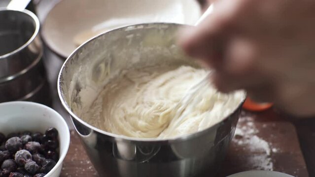 The pastry chef whips the dough for cupcakes with a whisk. Top view of the table with products. Cooking delicious confectionery at home