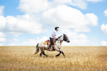 A young teenage girl gallops on a horse across a field, against the backdrop of a cloudy sky. Horse...