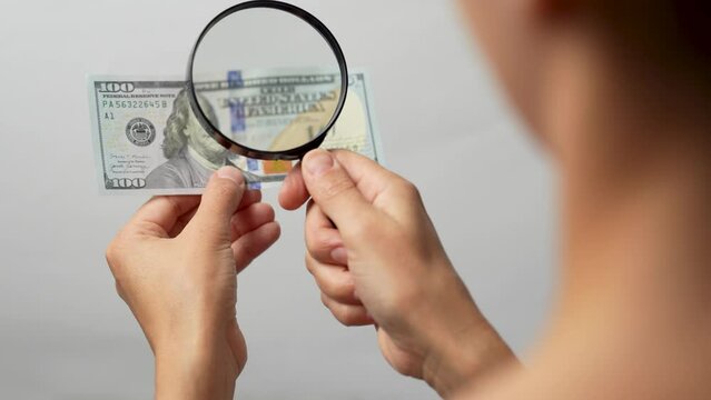 Woman checking hundred dollar bill with a magnifying glass