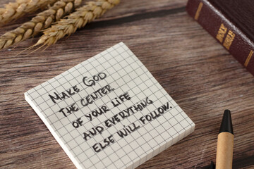 Handwritten inspiring quote with holy bible book and wheat stalk on wooden table. God is first...