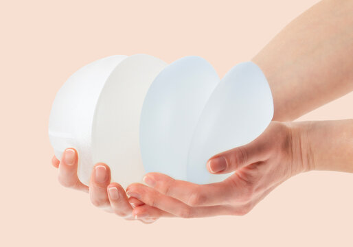  Female hands holding stack of different types of breast implants.