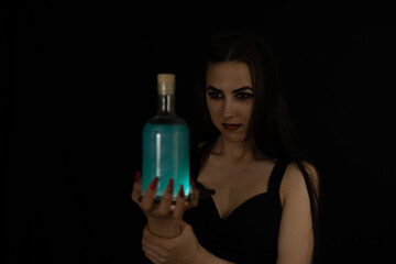 For Halloween, a beautiful witch brewed a potion. On a black background, a woman witch holds a...