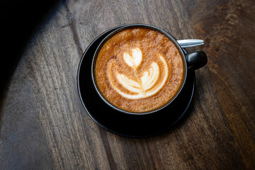 Hot coffee latte with latte art milk foam in cup mug on wood desk on top view. As breakfast In a coffee shop at the cafe,during business work concept,vintage style