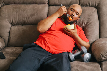 Lazy overweight man choose eating fruits rather than workout at home