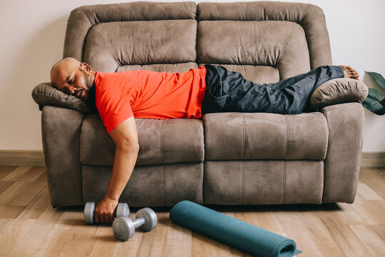 Lazy overweight man with dumbbells sleeping on sofa at home.