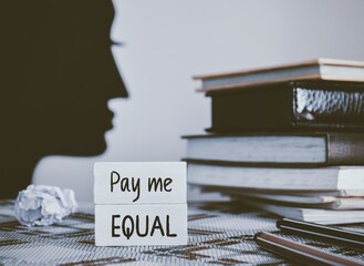 Pay Me Equal inscription on white chips on woman workplace. Gender wage gap concept.