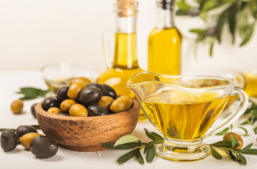 Olive oil in glass bowls, gravy boats and bottle on a textured kitchen table. Oil bottle with branches and fruits of olives. Place for text. copy space. cooking oil and salad dressing.Close-up.Flatley