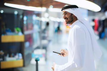 Full body of walking Arab man indoors. Emirati wearing Kandura inside a shopping mall or metro...