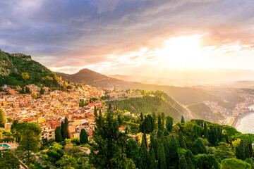 Fototapeta na wymiar travel landscape of a highland mediterranean town with yellow buildings, green trees and gardens, beautiful mountains and amazing cloudy sunset