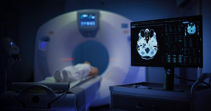 Medium Shot of a Female Patient Lying on a CT or MRI Scan, Bed is Moving Inside the Machine While it Scans her Brain. Display Showing the Results. Footage In Medical Laboratory or Healthcare Facility