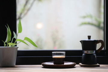 Coffee glass cup and black moka pot in front of window