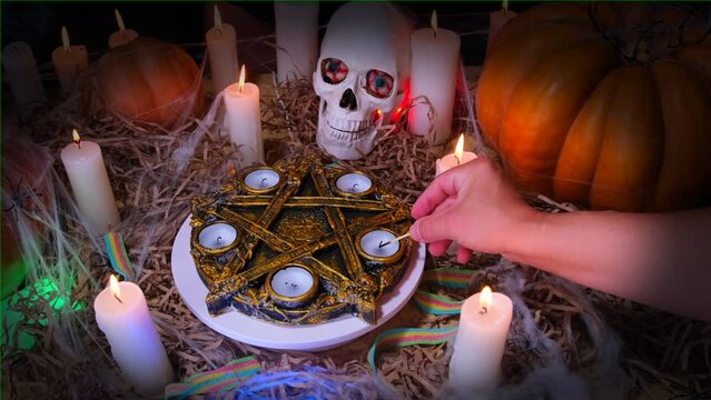 Mystical Halloween celebration background, a hand lights candles around a ritual pentagram, beautiful orange pumpkins and a skull in a cobweb. Trick or treat game, traditional autumn decorations.