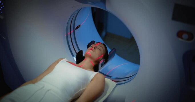 Close-up Portrait of a Female Patient Lying on a CT or MRI Scan, Bed is Moving Inside the Machine While it Scans Her Body and Brain with Red Laser. Footage In Medical Laboratory or Healthcare Facility