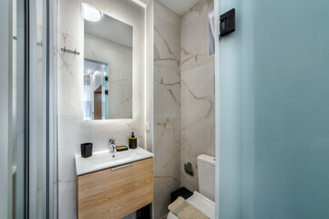 Modern bathroom with sink with wooden cabinet, toilet, mirror with light, grey colors. Interior design of hotel or apartment or home.