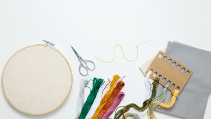Embroidery set fot stitching. Beige cotton cloth in embroidery hoop on white background with fabric, colorful threads, scissors and needls. Indoor hobby concept with copy space, top view © matucha12