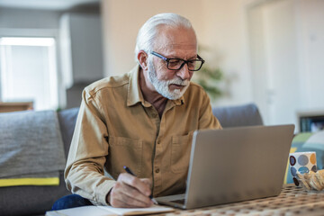 Fototapeta premium Shot of a senior man using a laptop while going over his bills and finances at home. Cropped shot of a senior man going through his finances while sitting at the dining room table.