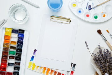 Watercolor and other artistic accessories on a white background. Artist's desk workplace. Top view,...
