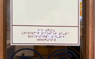 A plate displaying store opening hours in Braille font.