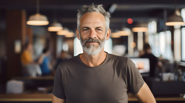 portrait of creative older man at work wearing a brown tshirt and jeans smiling to camera in casual office	