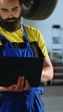Vertical video Licensed mechanic standing underneath suspended car in garage workspace using laptop to order new parts after finding issues. Employee looking online for replacing components using