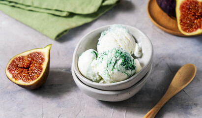 Figs ice cream in a ceramic bowls with fresh figs over grey background, green napkin, wooden spoon. Top view