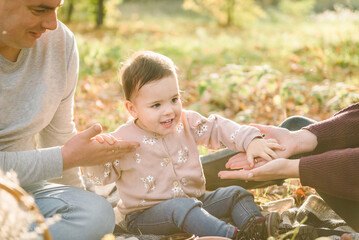 Autumn mood. Mother, father, kid have picnic in autumn forest in nature. Mom, dad hugs daughter child sitting on blanket on yellow leaves in park. Family spending time together at sunset on vacation.