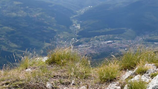 Grass swings in wind on mountain edge in selective focus, against valley