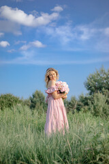 Fototapeta na wymiar Vertical image. Beautiful woman in pink summer sundress with large bouquet of peonies stands .