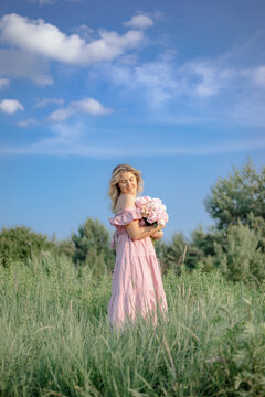 Vertical image. Beautiful woman in pink summer sundress with large bouquet of peonies stands .