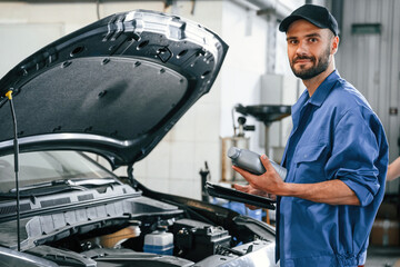 Grey colored oil can in hands. Auto mechanic working in garage. Repair service