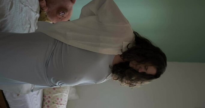 Vertical video, a pregnant woman with a big belly gets out of bed and feels pain and tension in her back. Caring for women who are pregnant. Third trimester, expecting the birth of a child.